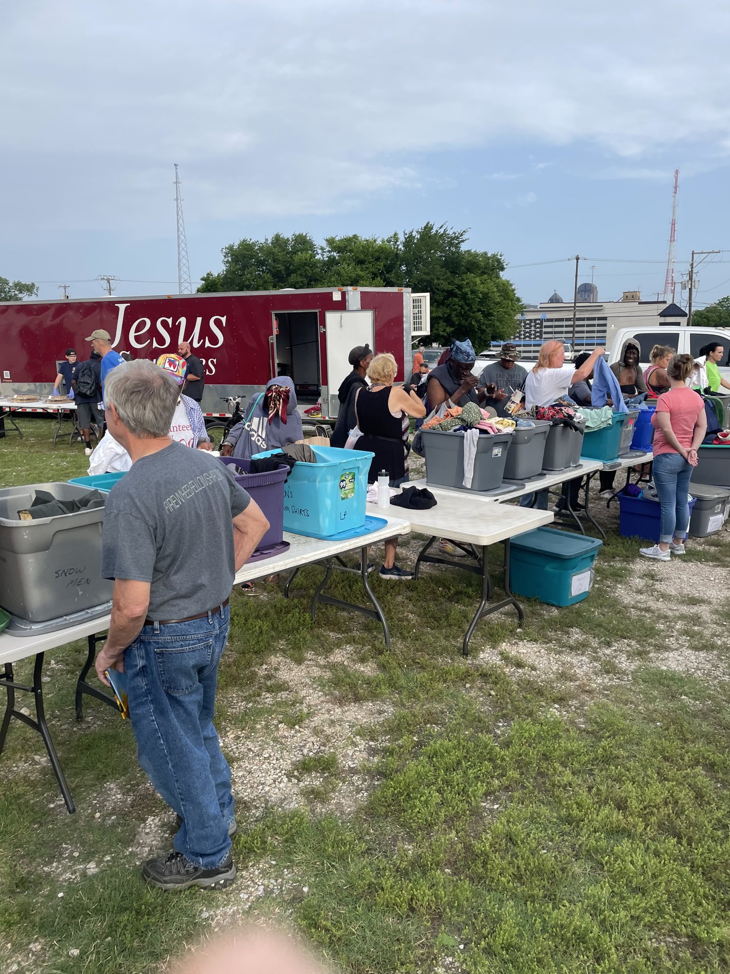 Volunteers at tables of clothes and supplies beside the Jesus trailer at a homeless outreach